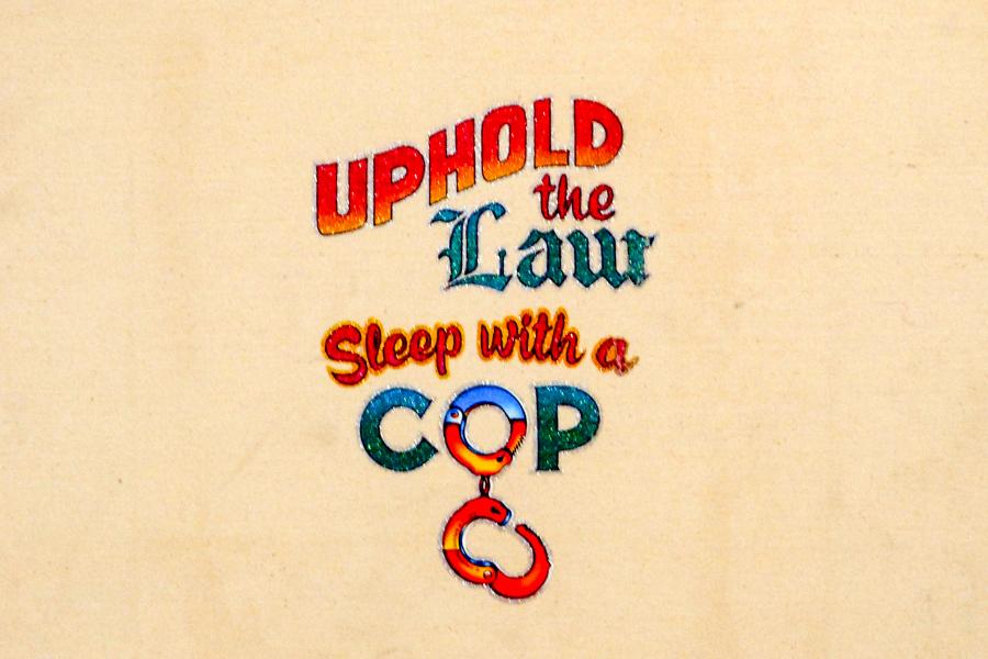 Close-up of a text-based artwork reading “UPHOLD the Law Sleep with a COP” on a light background.