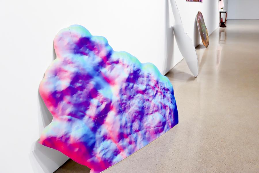 Freestanding cloud-shaped artwork installed along a gallery wall.
