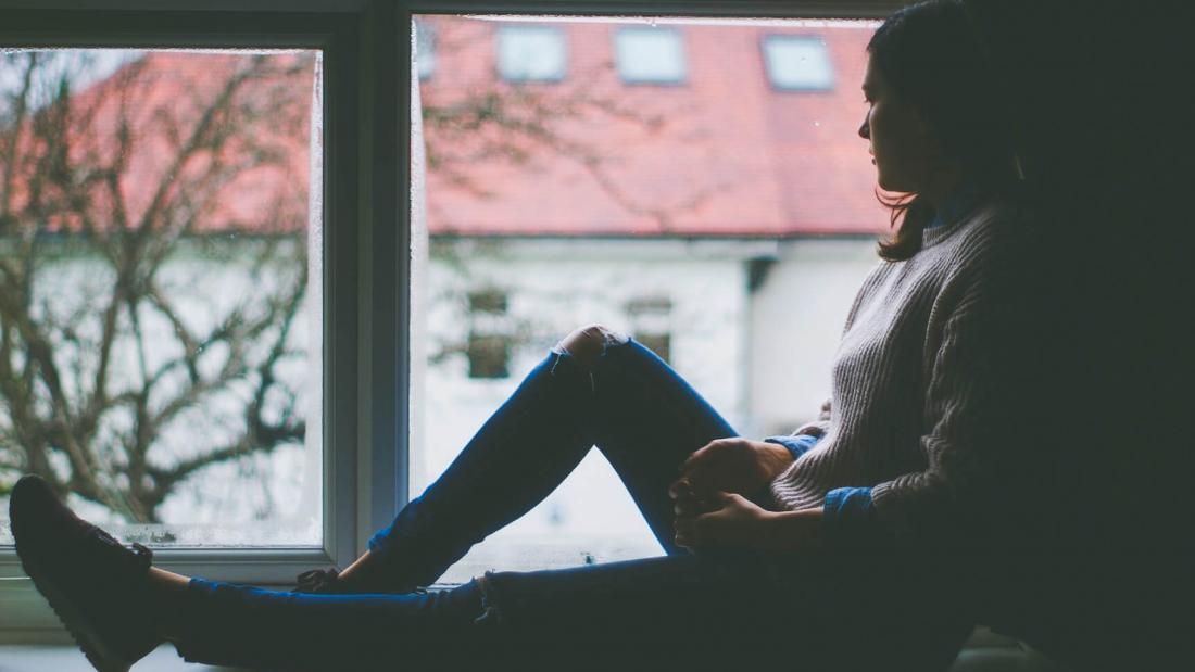 A person is seated at a window looking outside.