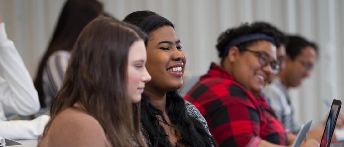 Students seated in a row, smiling during a lecture.