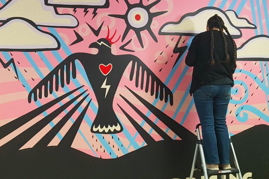 An indigenous artist works on painting a large mural.
