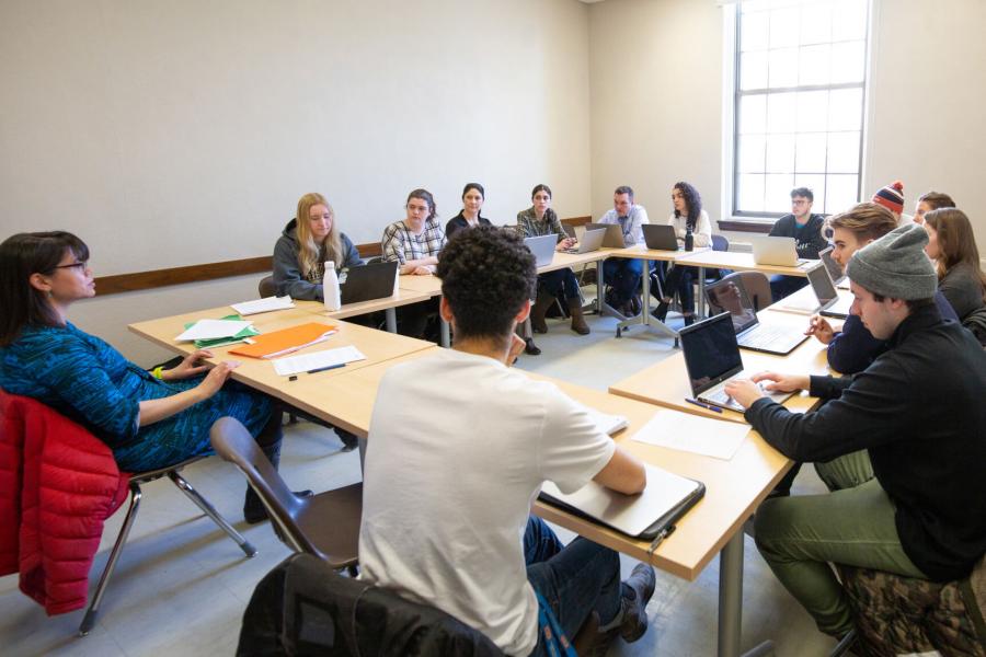 A classroom of students seated at long tables shaped in a square.