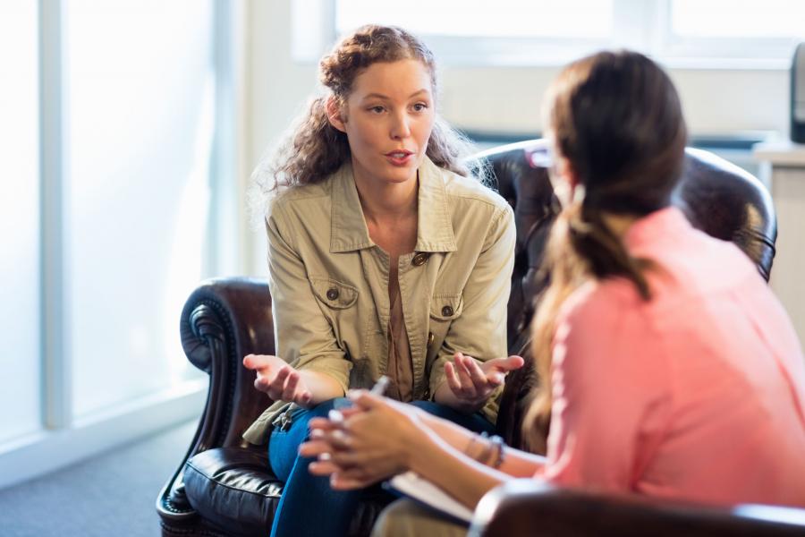 Two women facing each other on large leather chairs having a close discussion.