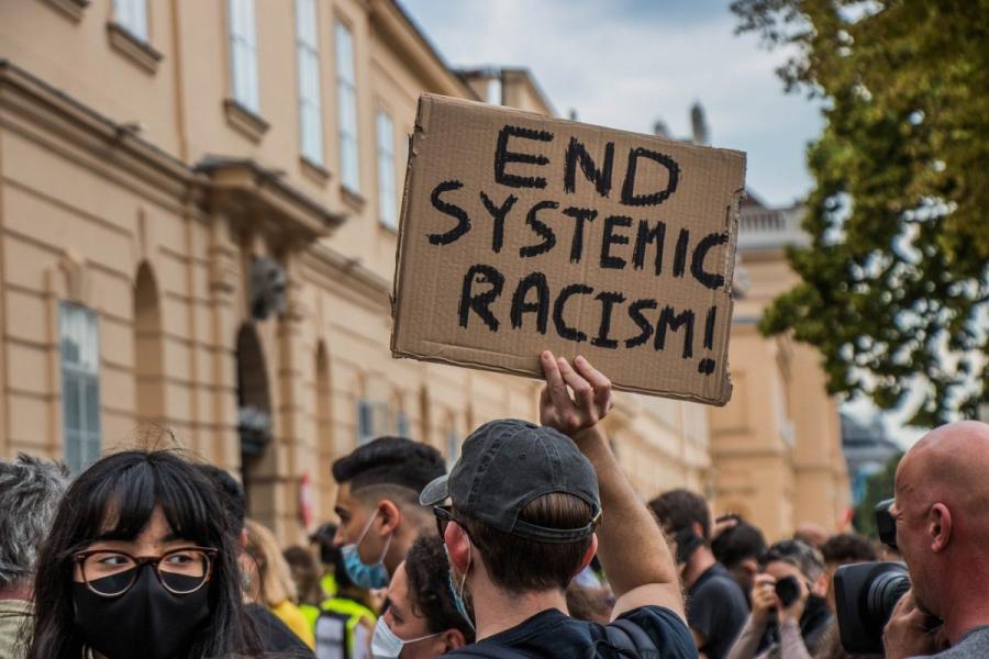Public demonstration with man holding up a homemade, cardboard sign reading "end systemic racism".