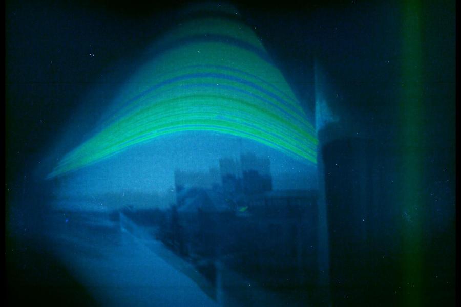 A digitized rendering of a swoosh of green lines over a dark blue sky, with a number of blurry buildings underneath.