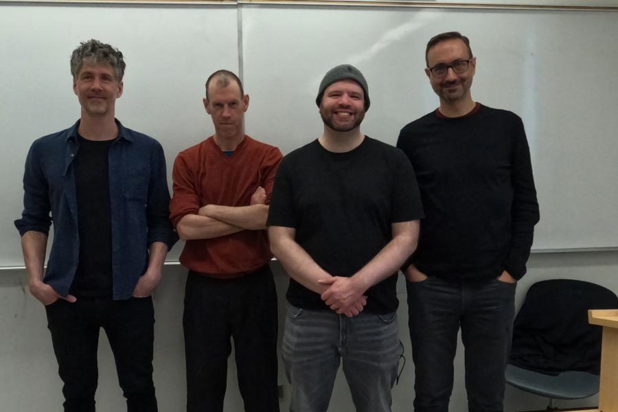 Four men standing in front of a whiteboard in a classroom, smiling at the camera.