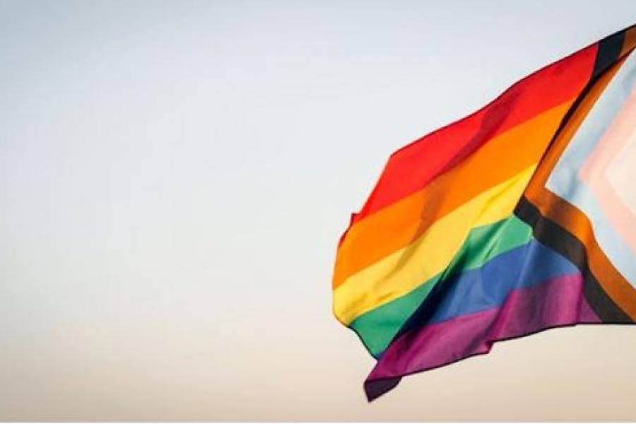 A rainbow pride flag against a clear sky.