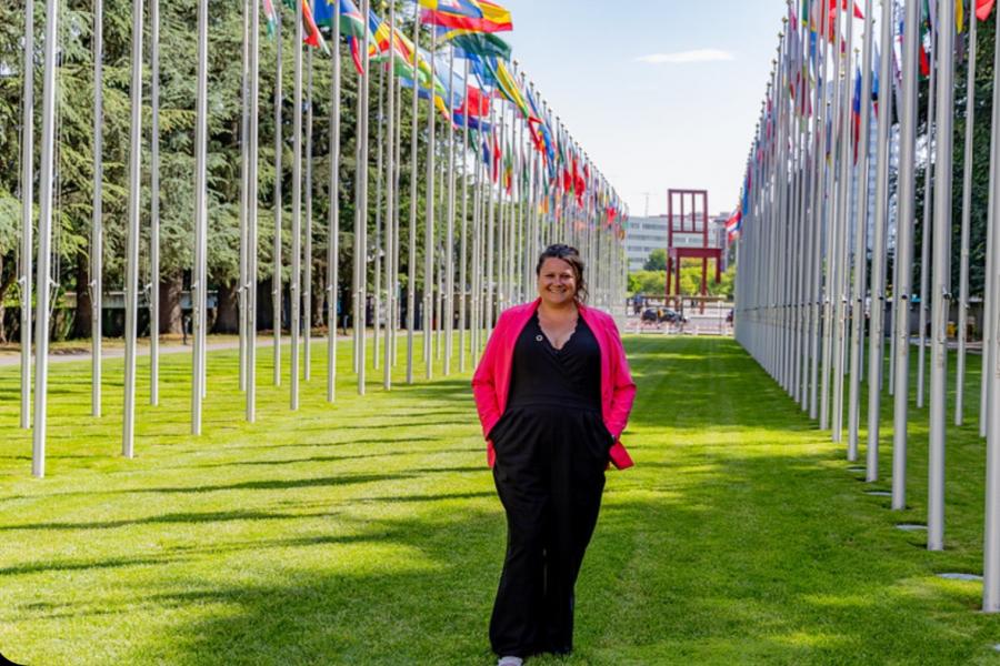 A woman standing in a grassy area with two rows of large white flagpoles on either side of her.