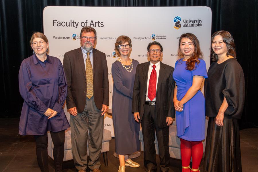 Group of six people posing in front of a Faculty of Arts backdrop.