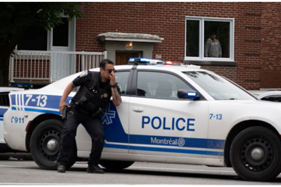 A policeman in uniform crouching down next to a marked police vehicle with lights flashing.