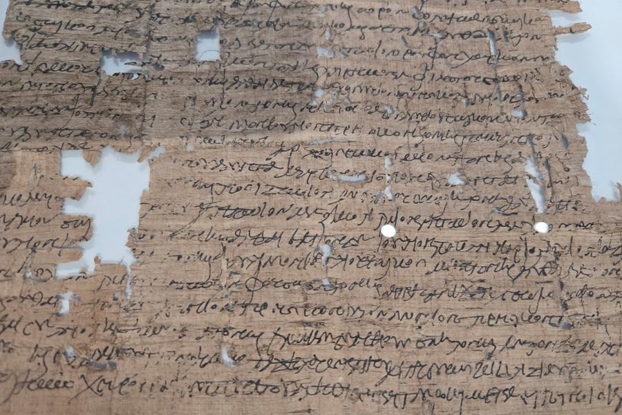 A fragile papyrus document with holes and rips and ancient greek cursive writing on it.