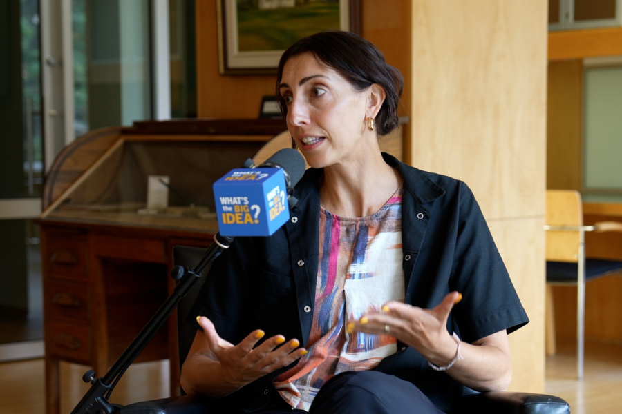 A woman sitting in front of a podcast microphone, with her hands open to the ceiling.