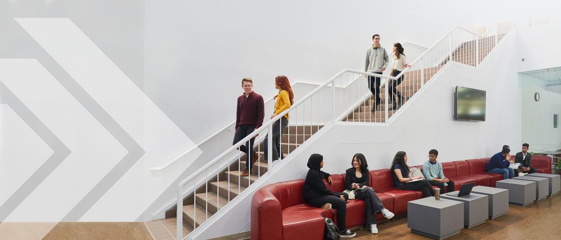 Students at the Asper School of Business in the atrium, some sitting on couches and walking down the staircase. 