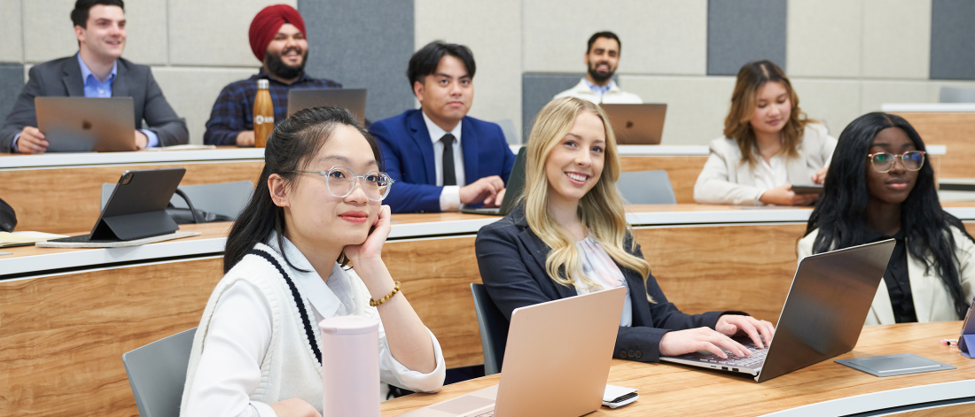 Students smiling in a classroom wearing business casual clothes at the Asper School of Business.