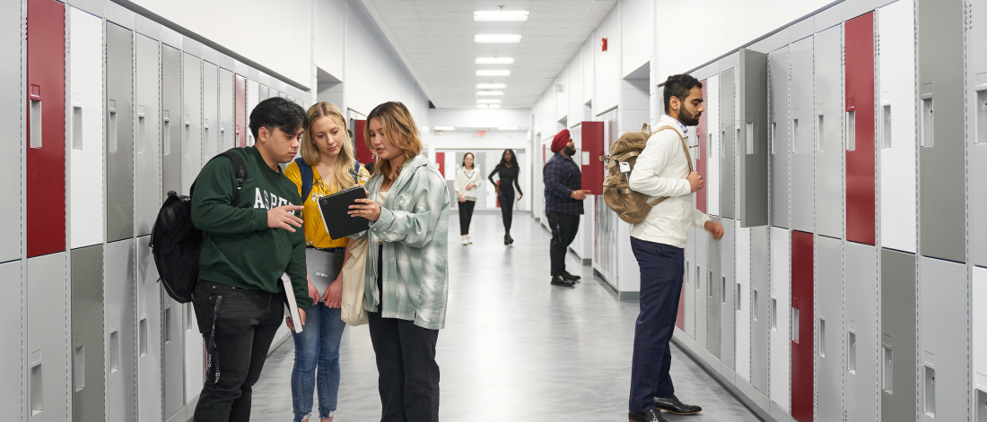 Students walking and talking in a hallway full of red, grey, and white lockers at the Asper Drake Centre.