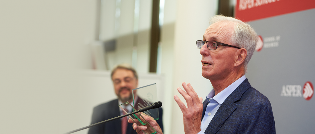 Male researcher winning an award with someone watching in the background.