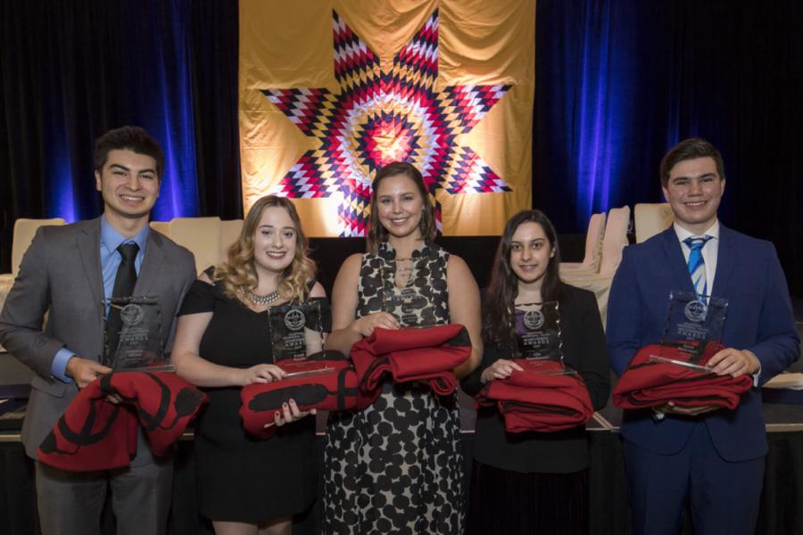 Five Indigenous Commerce Students stand side by side holding folded red blankets.