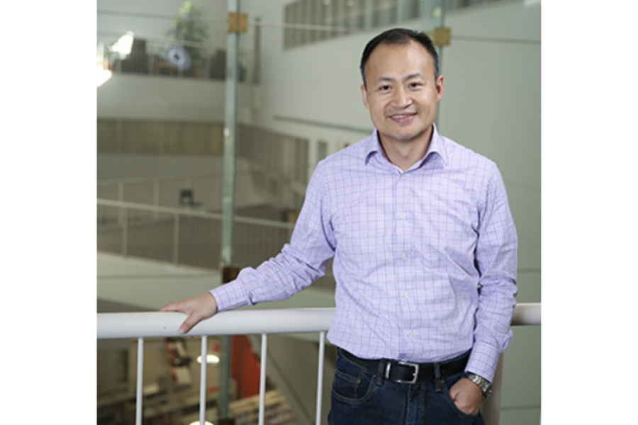 photo of professor Steven Zheng taken on the third floor of Drake Centre. One hand in his jean pocket, he leans on the balcony. He wears a light purple shirt.