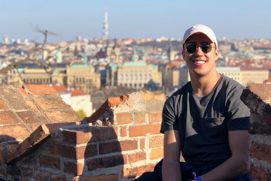 photo of a male student sitting on a ancient brick wall in Europe