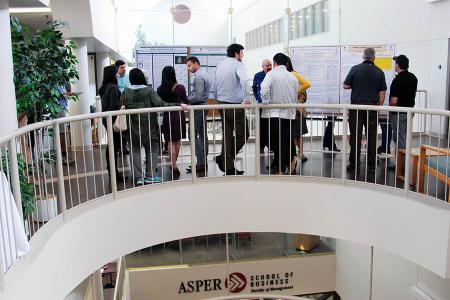 People looking at posters for a research event at the Asper Drake building.