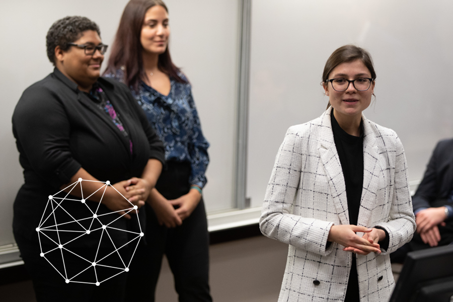 Three women standing at the front of a classroom, one appears to be talking to the audience (not visible).