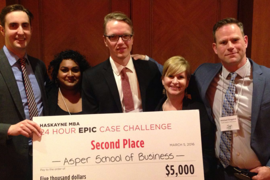 a group of three male students and two female coaches holding a winning cheque of $5000