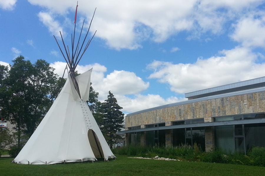 a white tipi tent on green grass and with blue sky in the background