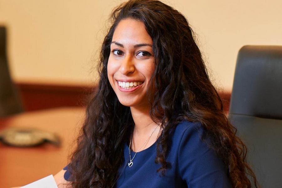 Asper School of Business female student sitting at table, wearing blue shirt, smiling.
