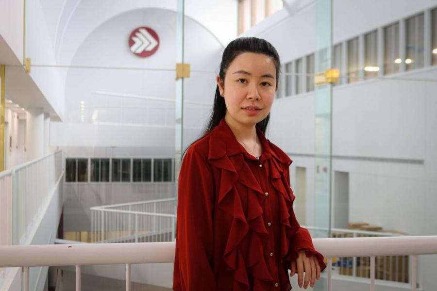 Sirius Zhang, wearing a red shirt leaning on a rail inside the Asper School of Business.