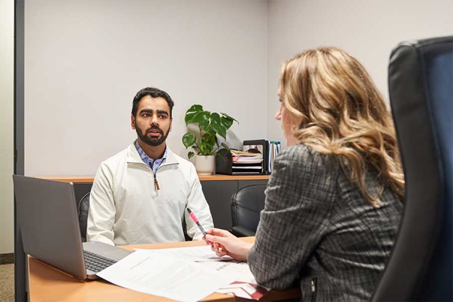 Male Asper student wearing white sweater meeting with an Asper staff member at a desk.