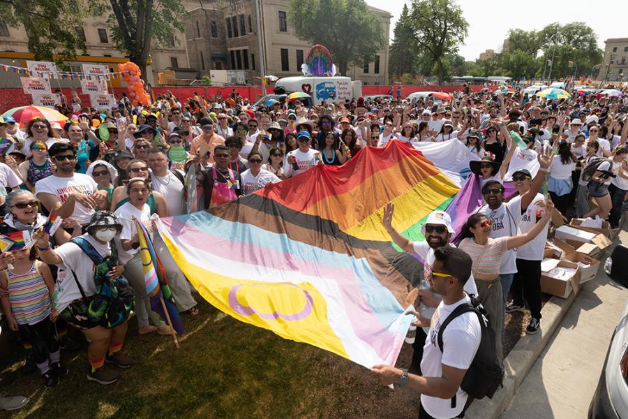 U of M community members gathered around a Pride Flag getting ready for the Winnipeg Pride Parade.