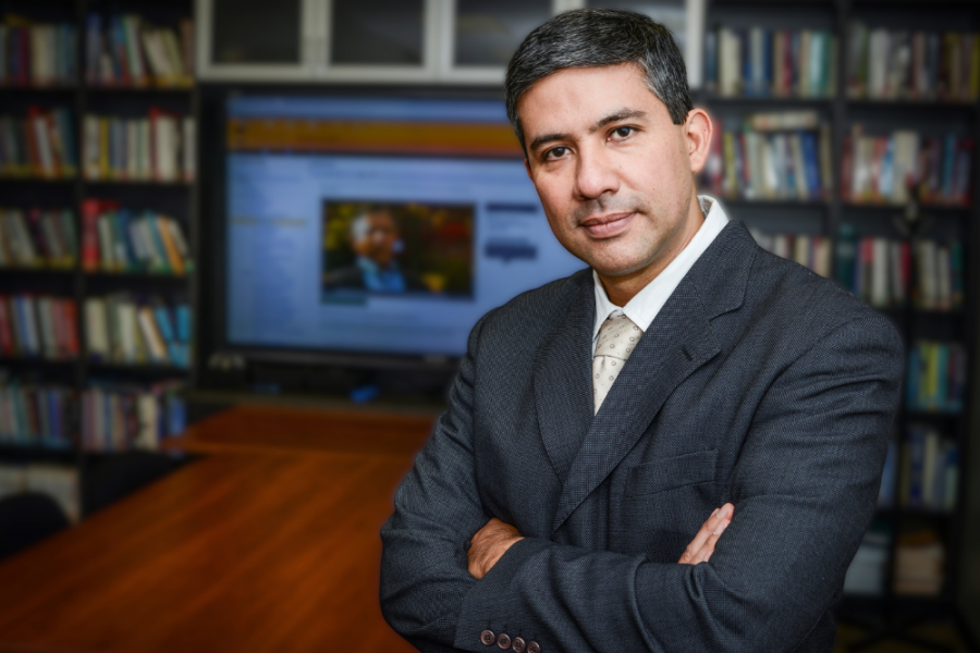 Image of a Hispanic man standing in front of a computer and books.