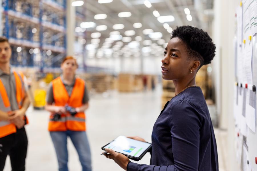 A black woman is speaking to a group of people in a warehouse setting.