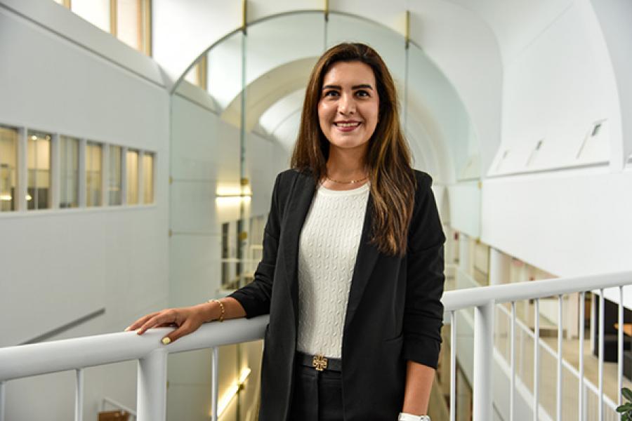 Kimia Ansari, Asper School of Business, standing in atrium wearing business clothes smiling.