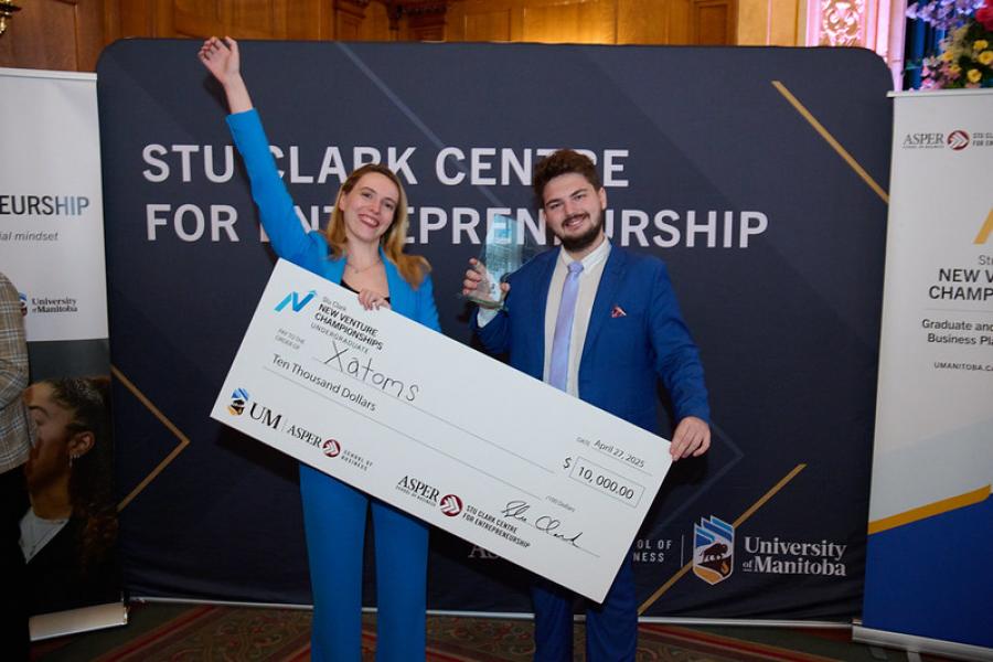 Two students celebrating, holding a big cheque from the Stu Clark Centre.