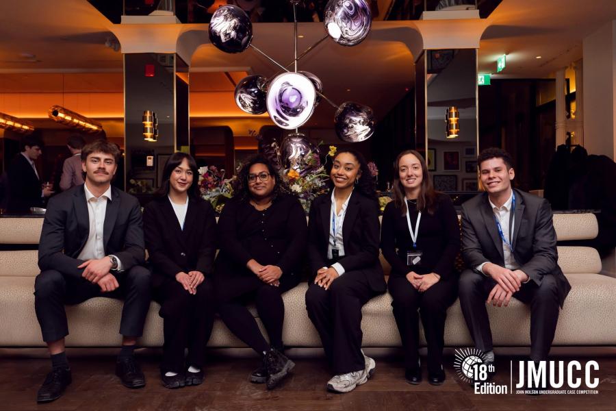 Five people in business casual sit on a bit and face the camera.