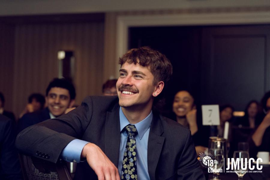 A man at a dinner in formal attire sits to face the presenter