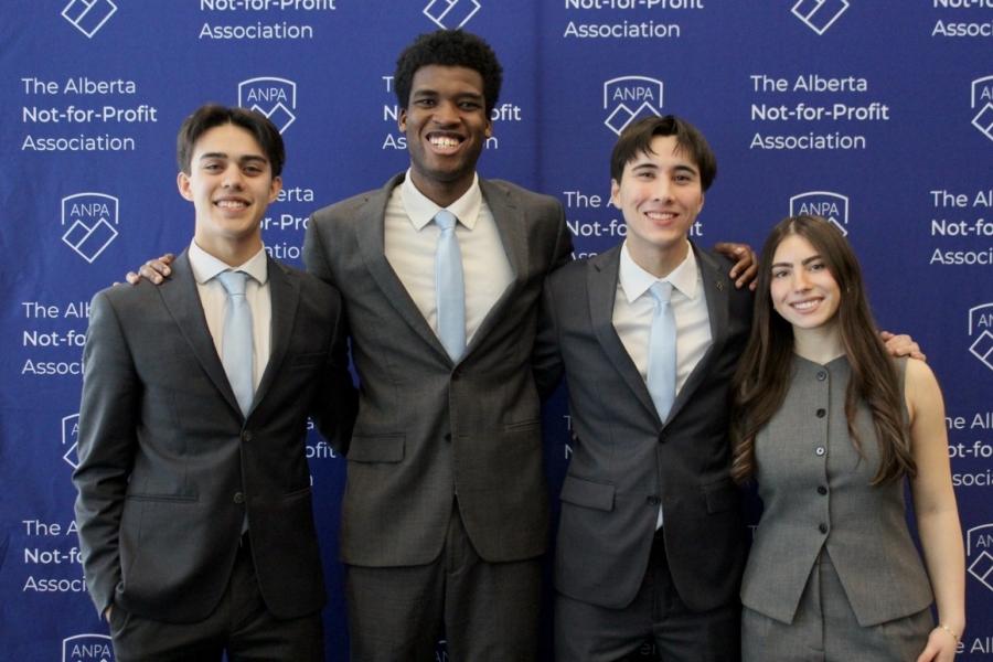 Four students stand together and pose for a photo in suits.