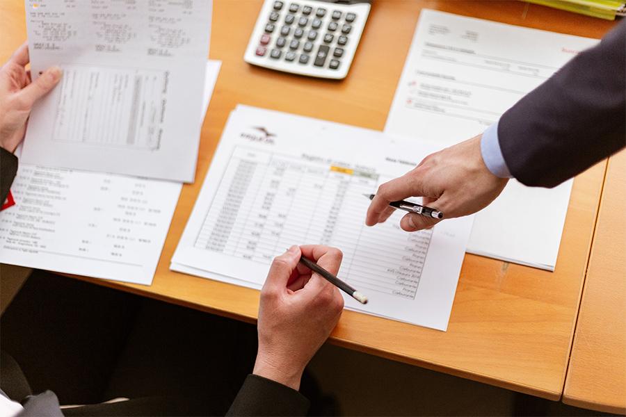 Two hands holding pens pointing at documents on a table.