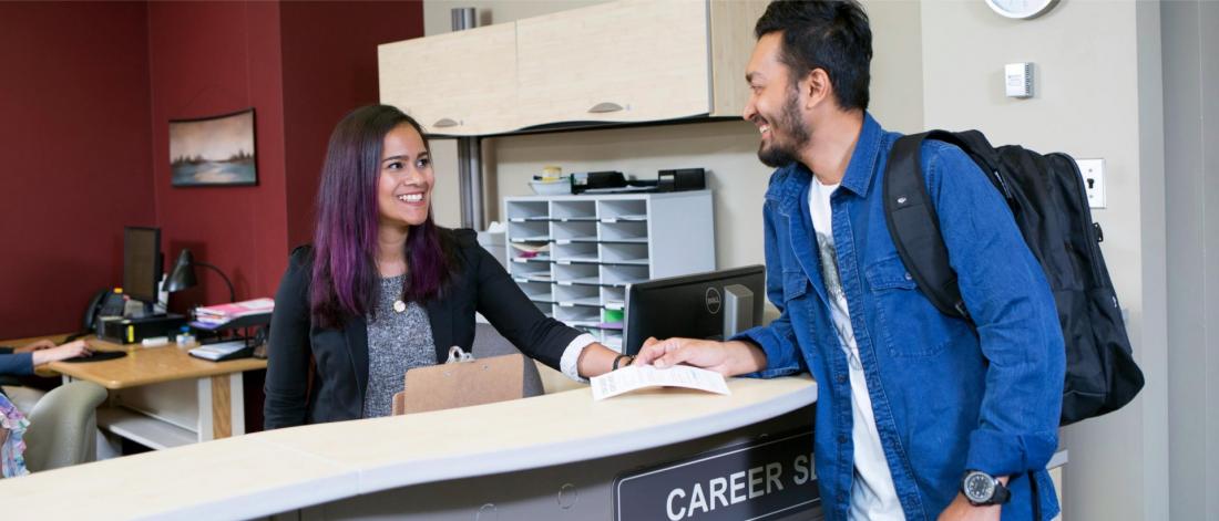 A career services staff member assists a student at the front desk.