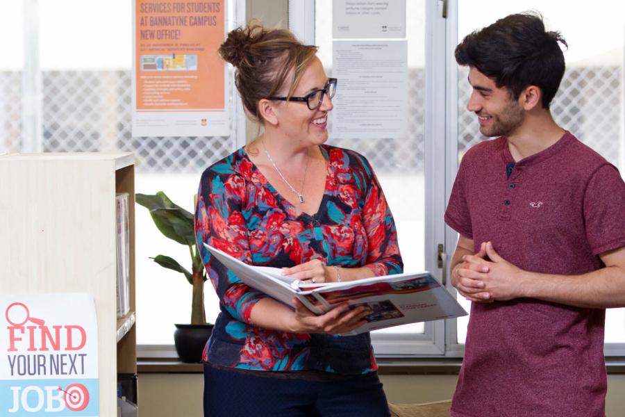 A University mentor stands holding a binder while providing career information to a student.