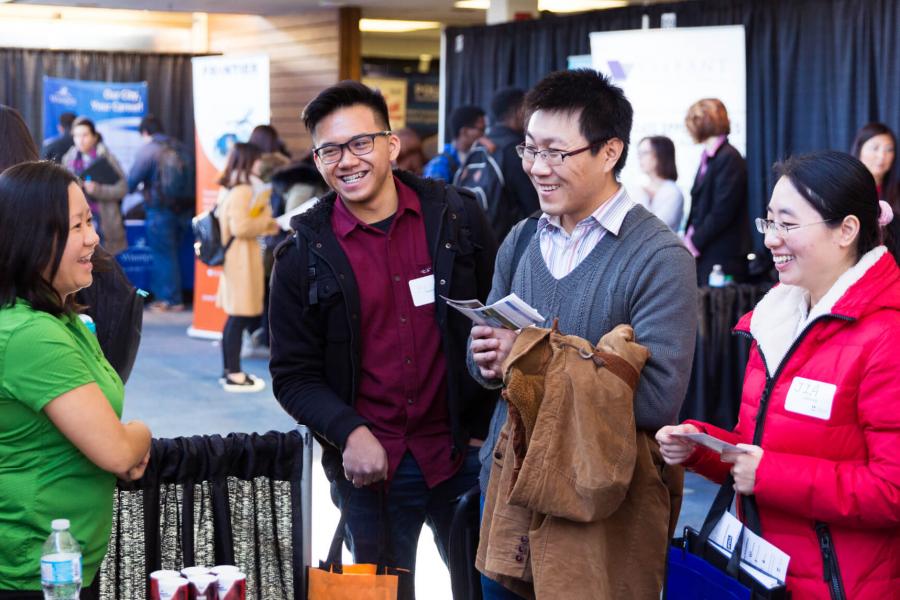 Three students chat with a potential employer at a career fair display booth.