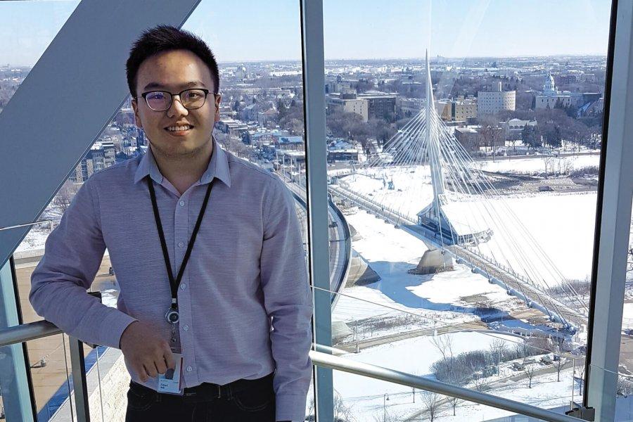 A student stands at an upper window of the Canadian Museum of Human Rights, the Winnipeg skyline behind him.