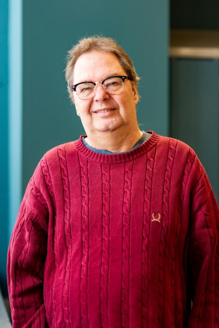 Portrait of man wearing a red sweater and glasses, with a blue wall in the background.