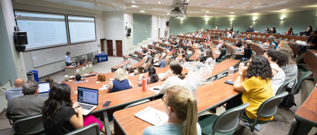 Full amphitheatre classroom looking at a PowerPoint presentation