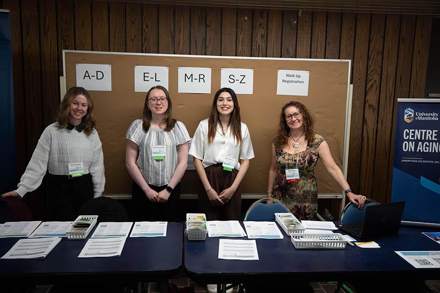Three students and Centre staff pose for a photo at the Symposium registration table.