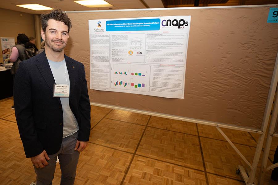 A graduate student stands beside his poster presentation at the 41st Spring Research Symposium
