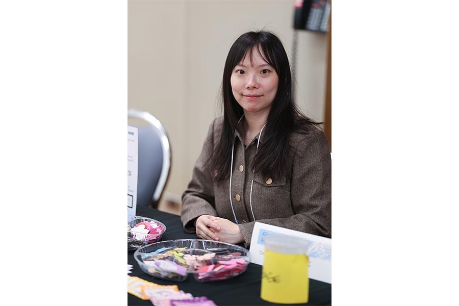 A student volunteer is seated at a table assisting with a craft project for Symposium attendees