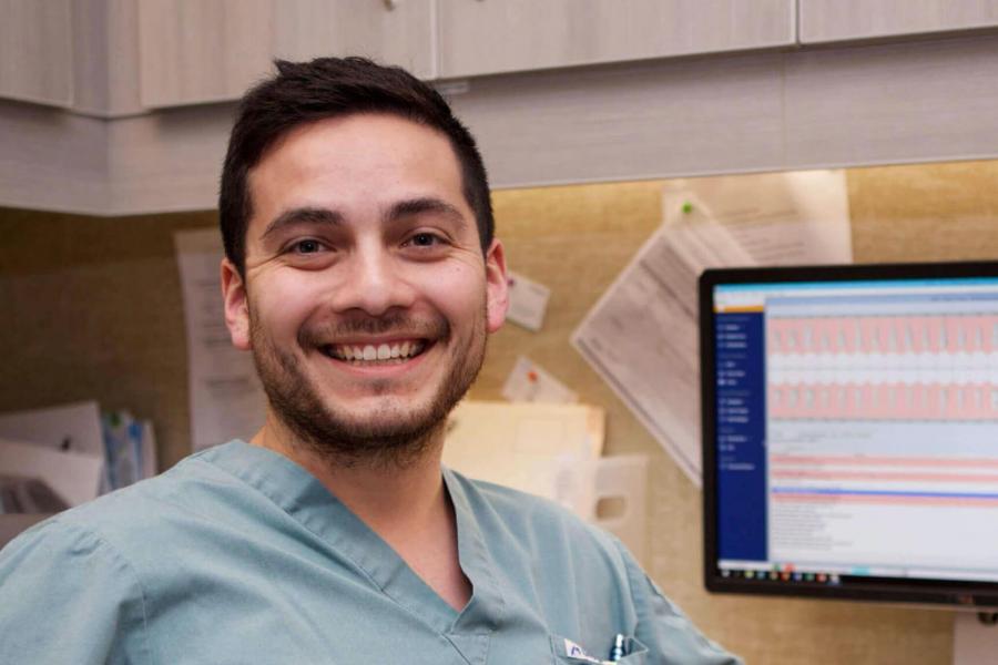 A college of dentistry student smiles as he sits at a desk with a computer work station.
