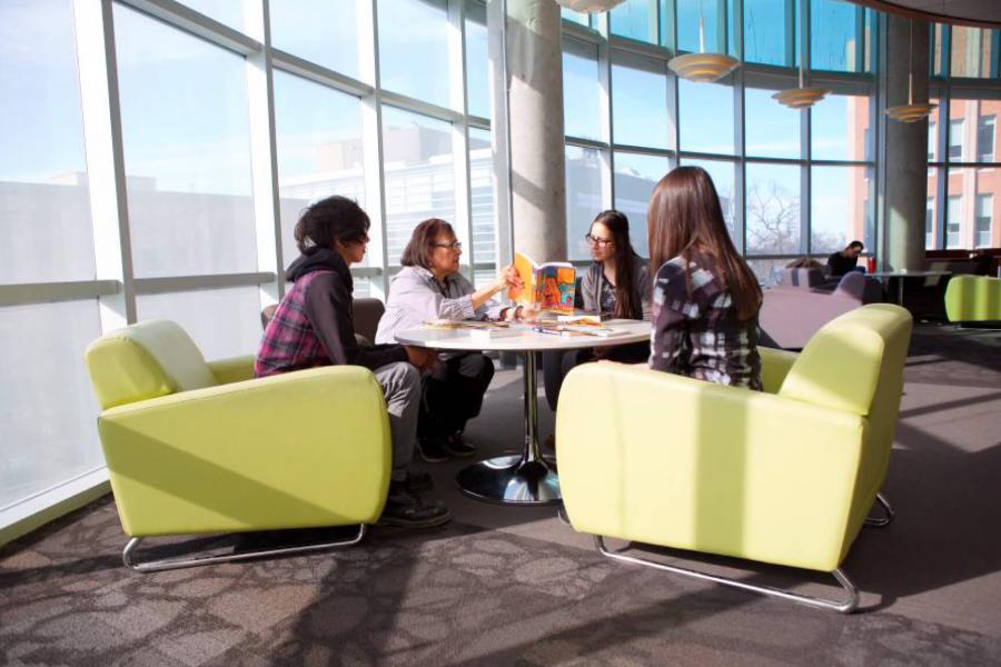 Four people sit around a circular table and look at books together.